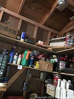 Shelves with assorted chemicals, spray bottles, and boxes in a wooden garage setting.