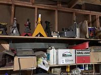 Shelf with multiple jack stands on top and boxes underneath, including a white plastic container and a red box labeled Grainger.