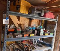 Three metal shelves holding yellow and red toolboxes, multiple small parts boxes, and fastener containers. Lower shelf and workbench display various hand tools including hammers and staple guns.