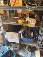 Full view of metal shelf containing various tools, cords, building supplies including box with clamps and wire basket