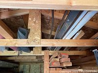 Wide view of shed roof area showing stacked lumber, metal rods, and structural framing