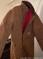 Brown Carhartt coveralls hanging, showing front side with collar and chest pocket and Carhartt logo patch.