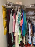Full view of closet rack filled with assorted vintage women's clothing including dresses, coats, tops, and skirts in various colors and patterns.