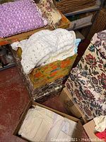 Stack of crocheted blankets on top of floral box with additional fabric linens below