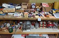 Overview of two shelves filled with various boxes, cans, tools, and hardware items spread out across the workspace bench and shelves.