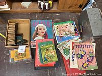 Photo showing assembled collection of vintage children's books, postcard albums, and ephemera items on floor.