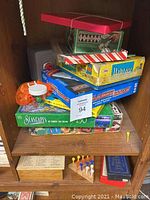 Stack of multiple board games including MahJong, Seascope, Ladder Golf, and others inside a wooden cubicle