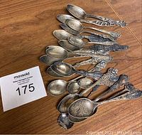 Fifteen tarnished sterling souvenir spoons fanned on wood surface with lot number card