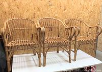 3 vintage bamboo chairs with rattan strapping arranged side by side on display table against plywood background