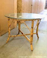 Full view of vintage bamboo table with rattan strapping and round clear glass top against warehouse background.