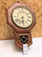 Full view of antique octagonal wooden school clock by Ansonia with pendulum door and key on display.