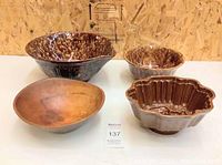 Four vintage bowls arranged on a white surface: two wooden and two ceramic brown mottled with scalloped edges. Visible wear and chips.