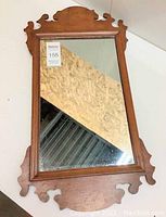 Full view of vintage wooden framed mirror laying flat showing mirror surface and wooden frame with decorative cutouts.
