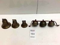Full set of seven antique brass bells, four mounted on metal bar and three standalone