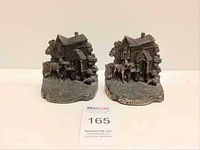 Pair of antique bronze bookends showing cottage and dog figures, placed side by side on a white background for scale and detail visibility.