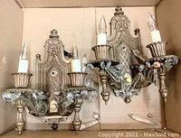 Pair of vintage brass wall sconces viewed from front in cardboard box, showing two candle-style bulbs each and decorative crystal accents.