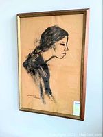 Framed ink wash portrait of a girl by Sylvia Lefkovitz viewed at an angle on a wall, showcasing the full artwork and frame.