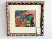 Front view of framed painting showing vibrant abstract art featuring a green face, cream mat, and ornate gold frame