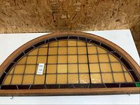 Full view of the arched stained glass transom window with an amber yellow glass pattern and wooden frame.