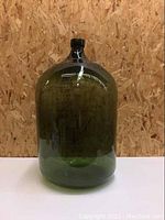 Front view of the large vintage hand-blown glass demijohn showing its green tint and rounded shape.