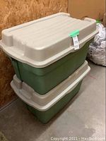 Two large Rubbermaid storage bins stacked with beige lids and green bodies, showing surface wear and scuffs.