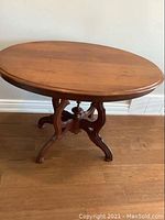 Front view of oval antique wooden table showing tabletop and pedestal base with curved legs.