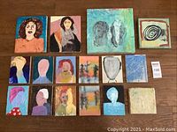 Full shot of all 15 encaustic wax mixed media artworks on wood laid out on floor, showing variety of portraits and abstract figures