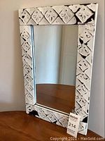 Front view of the rectangular mirror with its white distressed wooden frame decorated with a diamond patterned floral motif.