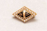 Front view of diamond-shaped gold sorority pin with black enamel center and seed pearl border.