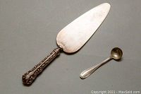 Cake cutter and monogrammed spoon arranged on a flat surface showing front view