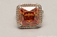 Close-up of square orange faceted stone ring with clear stone halo in rhodium plated silver.
