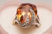 Front angle showing large orange faceted stone and clear accent stones on rhodium plated silver ring on heart shaped holder.