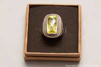Top down view of the ring in a brown jewelry box showing the yellow rectangular faceted gemstone and rope detail bezel.
