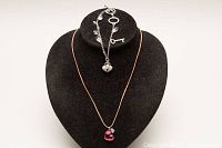 Photo of black display bust showing the necklace with pink heart pendant and charm bracelet arranged over it.