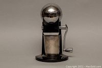 Front view of the Retro Metrokane Ice-O-Mat manual ice crusher, showing black base and chrome dome with embossed branding and crank handle on side.