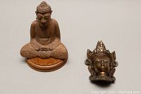 Top view of hand carved wooden seated Buddha statue and brass wall art figure's head side by side on flat surface