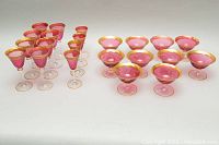 Full set arranged showing groupings of cranberry glass stemware with gold rims including tall narrow glasses and wider bowl glasses