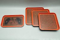 Four Asian lacquered trays arranged with three square trays stacked and smallest rectangular tray in front.