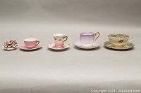 Front view of four teacup and saucer sets and a small porcelain floral bouquet decoration arranged in a row on white background.