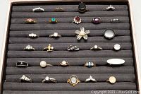 Top down view showing all 28 assorted costume rings organized in rows on gray felt with various stones and band styles.