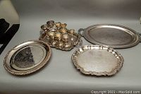 Photo showing multiple silver plated trays in various shapes and sizes along with a set of goblets