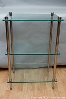 Front angled view of the three-tiered glass and chrome accent table, highlighting glass shelves and chrome leg details.