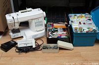 Brother XR-23 sewing machine with foot pedal, accessory box and container of sewing supplies on floor.