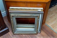 Four decorative wall frames displayed leaning against wood furniture on wood floor.