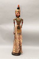 Front view of the 28.5-inch Asian shadow puppet on stand showing details of carved wooden head with crown and torso with fabric garment and fringes