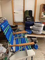 Three outdoor folding chairs with blue-green striped fabric and wooden armrests, set in a garage with camping gear around