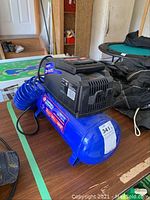 Blue Campbell Hausfeld air compressor with black top housing and attached air hose sitting on a table.