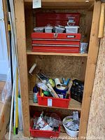 Red metal toolbox and three shelves with various garage supplies including plastic bins containing hardware and painting tools.