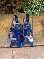 Four blue metal axle stands with handles and adjustable jaws, shown from front and top angles.