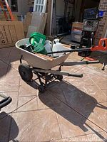 Side view of resin wheelbarrow with garden tools visible inside, including green Mastercraft chainsaw and white sprayer